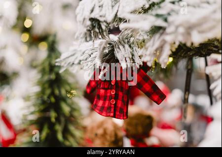 Un piccolo cappotto a quadri rosso e nero è appeso a un ramo d'albero. Il cappotto è realizzato in tessuto e presenta bottoni sul davanti Foto Stock