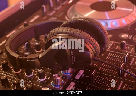 Cuffie che poggiano su una console di mixaggio DJ con una calda illuminazione del palcoscenico, simboleggiano la produzione musicale, la performance dei DJ e la cultura della vita notturna. Foto Stock