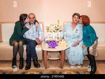 Una famiglia russa che celebra un anniversario di matrimonio d'oro in un ufficio di registro. Il marito e la moglie si siedono insieme con le medaglie, circondati dal loro dau Foto Stock