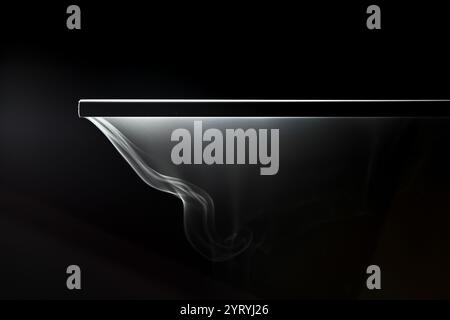 Il fumo bianco che scorre delicatamente da una superficie metallica crea un bellissimo motivo astratto su uno sfondo nero Foto Stock