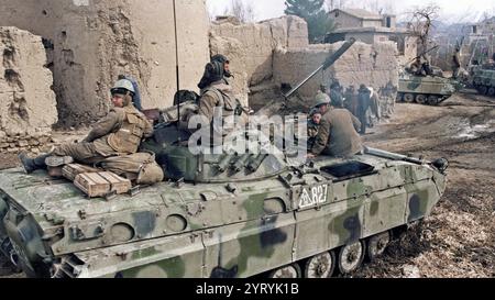 I soldati sovietici cavalcano in cima a un carro armato attraverso un villaggio afghano il 23 febbraio 1988. Foto Stock