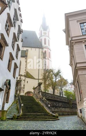 Una vista mistica autunnale della Chiesa di San Vito a Cesky Krumlov, con la sua guglia avvolta dalla nebbia, che crea una scena suggestiva e senza tempo nella Foto Stock