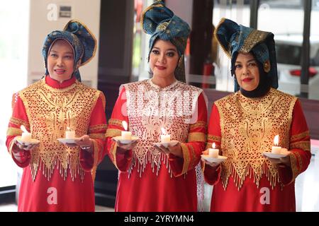 Tre donne in abiti Minangkabau rossi e dorati partecipano a un rituale, il soffice lume di candela che riflette il ricco patrimonio culturale. Foto Stock