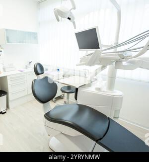 Studio dentista luminoso e moderno, dotato di apparecchiature professionali, una comoda sedia e un monitor, per creare un'atmosfera pulita e invitante Foto Stock