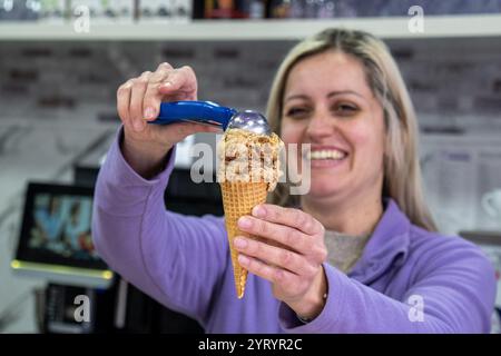 Treviri, Germania. 4 dicembre 2024. La proprietaria della gelateria Svetlana Novoselska organizza un gelato speculoos su una paletta di tiramisù durante la stagione dell'Avvento. Il suo negozio rimane aperto anche in inverno e offre waffle, crêpes, torte e bevande calde. Credito: Harald Tittel/dpa/Alamy Live News Foto Stock