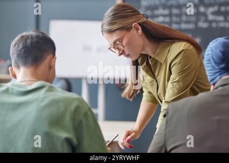 Immagine media di una giovane insegnante donna in piedi accanto a una studentessa adulta alla scrivania che spiega l'attività a casa alla fine della lezione nella scuola di lingua inglese, copia spazio Foto Stock