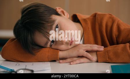 Scolaro caucasico annoiato sonnolento a scuola istruzione elementare studio di apprendimento stanco stanco triste turbato affaticato bambino ragazzo allievo scolaro Foto Stock