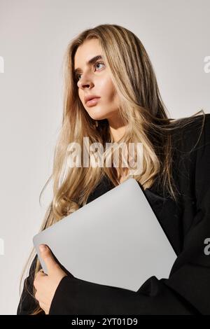 Una bella giovane donna indossa elegantemente un abito nero, tenendo in mano un notebook in uno studio. Foto Stock