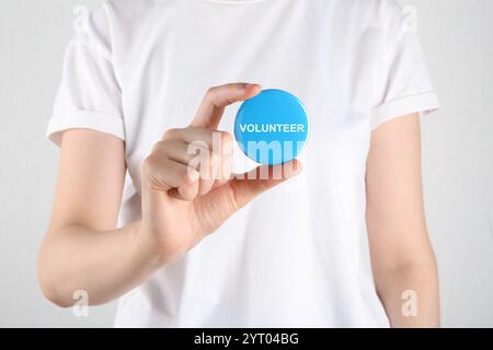 Donna che tiene in mano un distintivo con la parola Volunteer su sfondo bianco, primo piano Foto Stock