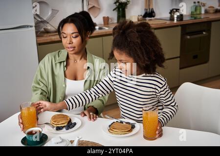Mamma e sua figlia si siedono ad un accogliente tavolo da cucina, assaporando pancake e succo di frutta insieme. Foto Stock