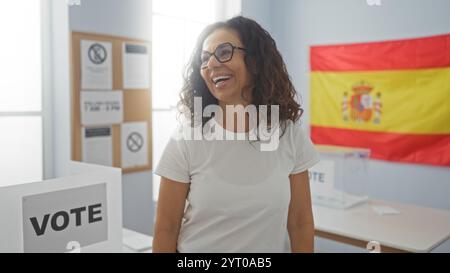 Donna sorridente in un seggio elettorale in spagna con una bandiera spagnola sullo sfondo, indicata dal segno di voto e dai manifesti elettorali esposti in casa Foto Stock