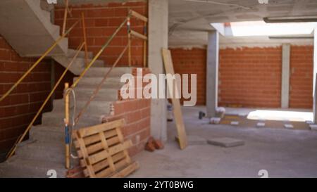 Immagine sfocata di un cantiere non finito con pareti in mattoni, pavimenti in cemento e materiali da costruzione sparsi, con scale parzialmente costruite Foto Stock