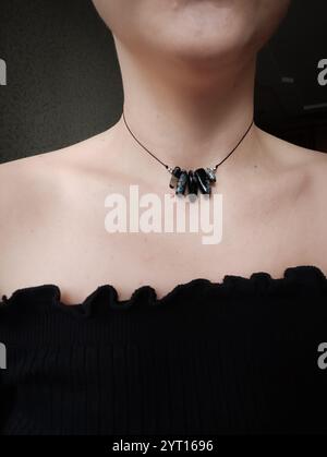 Pietra preziosa in agata nera con filtro blu. Collana nera con cordoncino irregolare sul collo della donna. Gioielli in pietra naturale, gioielli con perline Foto Stock