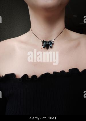 Pietra preziosa in agata nera con filtro blu. Collana nera con cordoncino irregolare sul collo della donna. Gioielli in pietra naturale, gioielli con perline Foto Stock