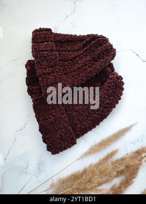 Cappello a maglia, berretto di cioccolato marrone scuro su sfondo in marmo bianco, vista dall'alto, piatto, velluto, uncinetto, coppia, set, copricapo autunnale invernale Foto Stock