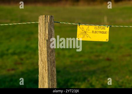 Pannello di recinzione elettrica nella campagna francese. Il cartello avverte i visitatori dei pericoli della recinzione elettrica. Recinzione di sicurezza ad alta tensione Foto Stock