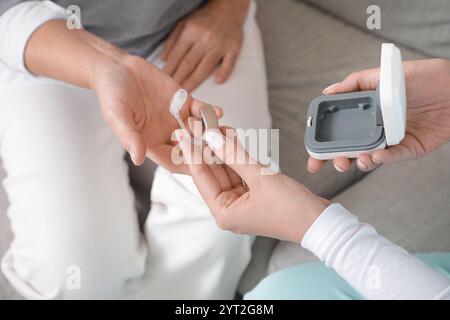 Medico che dà l'apparecchio acustico a una donna matura mentre la visita a casa, primo piano Foto Stock