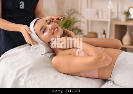 Giovane donna con cerotti sotto gli occhi che riceve un massaggio facciale nel salone di bellezza, primo piano Foto Stock