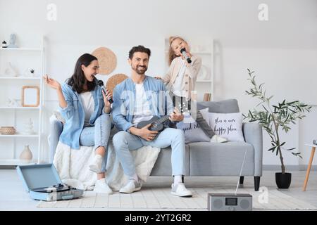 Famiglia felice con microfoni e ukulele che cantano karaoke a casa Foto Stock