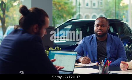 Venditore di auto che fornisce alla coppia la documentazione da leggere dopo aver concordato i termini. Agente che concede un contratto di vendita per i clienti da firmare dopo aver deciso di effettuare l'acquisto, fotocamera A. Foto Stock