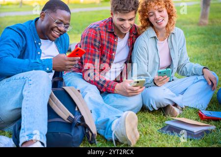 Gruppo di amici seduti sull'erba, utilizzando smartphone e divertendosi Foto Stock