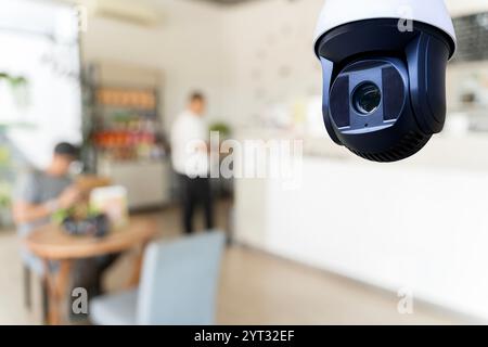 Una telecamera di sicurezza è appesa al soffitto di un caffè, con l'interno sfocato sullo sfondo. Telecamera di sicurezza che monitora la caffetteria moderna Foto Stock