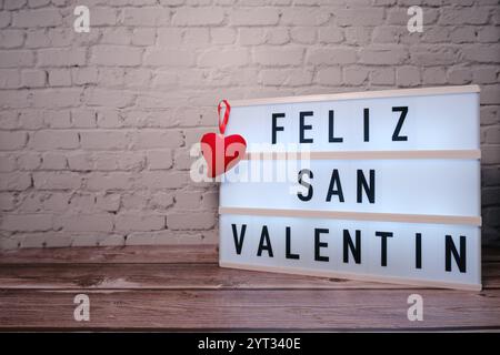 Scatola luminosa con testo "buon San Valentino" con cuore rosso su tavolo in legno e sfondo in mattoni Foto Stock