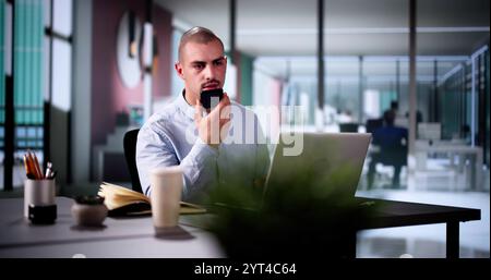 Uomo d'affari professionista che utilizza l'app per smartphone per le chiamate client in un ufficio moderno con laptop e sorridente Foto Stock