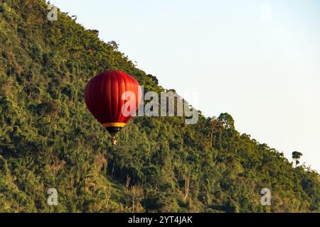 Red mongolfiere volare oltre la montagna e il verde campo di riso in Vang Vieng, Laos Foto Stock