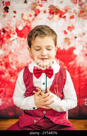 Gilet rosso e cravatta con le mani sopra il cuore e decorazioni a cuore Foto Stock