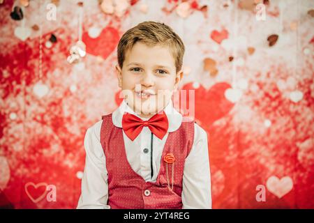 Ragazzo sorridente in gilet rosso e cravatta con sfondo cuore di San Valentino Foto Stock