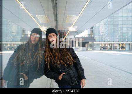 Giovane donna urbana appoggiata su un muro di vetro nella città moderna Foto Stock
