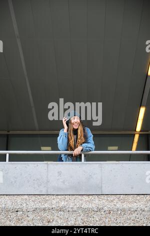 Giovane donna che ascolta la musica con le cuffie appoggiate alla ringhiera Foto Stock