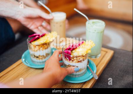 Mani che raggiungono dopo la Granola di frutta tropicale con latte Foto Stock