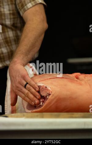 Un macellaio che ispeziona un lombo di maiale fresco durante una dimostrazione Foto Stock