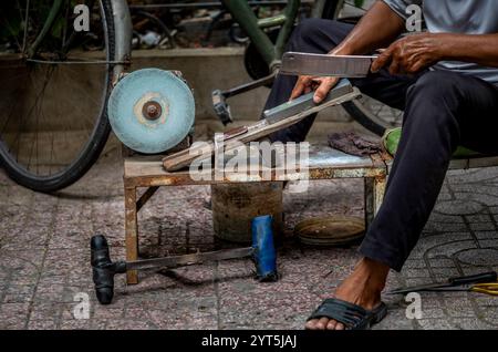Un uomo che affila i coltelli a mano per le strade di Saigon in Vietnam Foto Stock