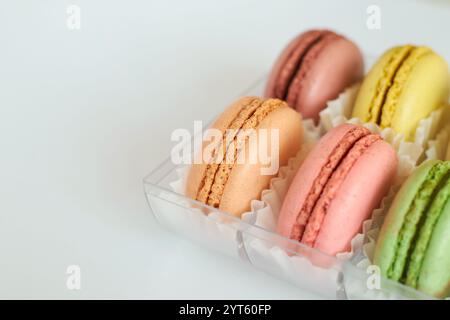 Delicati torte colorate, macaron francesi con carta bianca in scatola di imballaggio trasparente in plastica su sfondo grigio. dessert appetitoso, vari maca Foto Stock