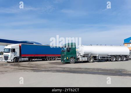 Due lunghi camion a dieci ruote, uno con rimorchio, parcheggiati nel parcheggio in una giornata di sole. Veicolo commerciale per il trasporto d'affari. Pubblicità Foto Stock