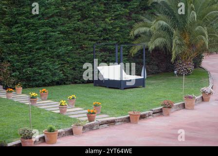 Madremanya, Spagna, 11 maggio 2013: Sereno patio in giardino con letto lounge e fiori in vaso Foto Stock