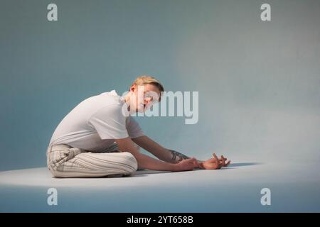 giovane uomo biondo con t-shirt bianca su sfondo blu, seduta a tutta lunghezza sul pavimento Foto Stock