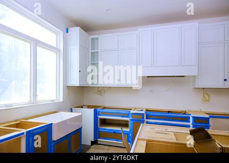 È in corso la costruzione di una nuova cucina con armadi bianchi che ospitano lavello e nastro di mascheratura blu per mobili non finiti per la massima protezione Foto Stock