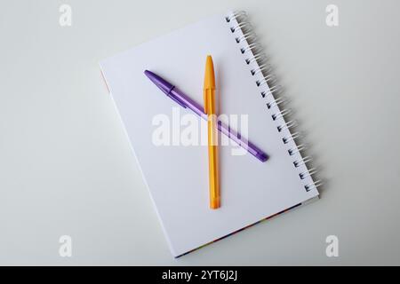 Quaderno di carta con pagina vuota e due penne colorate su sfondo bianco per i materiali scolastici. Cartoleria creativa, concetto di ritorno a scuola con spazio di copia. Foto Stock