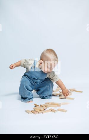 Simpatico ragazzo con salopette in denim su sfondo bianco. Bambini che giocano con giocattoli di legno. Bimbo sorridente di ottimo umore Foto Stock