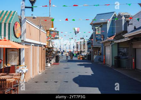 Bandiere colorate adornano la strada di Fisherman's Wharf, Monterey. Negozi e ristoranti pittoreschi, tra cui Pirate's Cove, fiancheggiano l'area sotto un blu chiaro Foto Stock