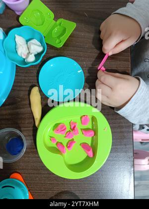 Il bambino modella la plastica morbida, gioca al tavolo con una serie di stampi e un coltello. Giochi educativi. Foto Stock