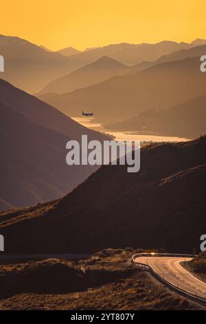 Vista dal Crowns Range sull'Isola del Sud in nuova Zelanda verso Queenstown. Il sole è appena tramontato e bagna il paesaggio con luce dorata. Un aereo sta volando sopra la valle durante il suo avvicinamento a Queenstown. Foto Stock