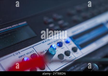 Una console di missaggio audio è mostrata in dettaglio, con sezioni etichettate come MAIN e AUX IN, con spie blu e rosse che indicano l'uso attivo. Foto Stock