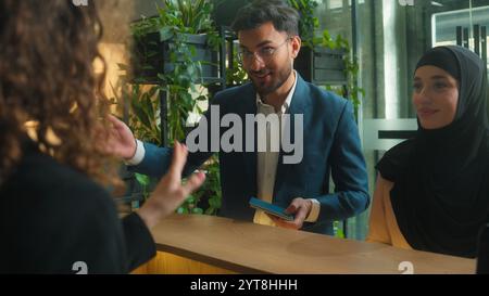 Arabo musulmano coppia uomo donna in hijab clienti turisti viaggi in famiglia vacanze viaggi ospiti felici arrivare prenotazione servizio hotel reception donna Foto Stock