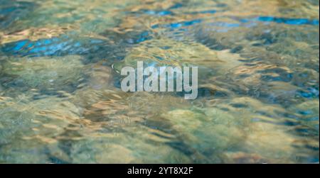 Inquadratura full frame con angolo basso che mostra una superficie d'acqua fluente con alcuni riflessi in un fiume poco profondo Foto Stock