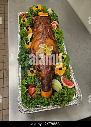 Maiale intero arrosto servito su un piatto decorativo circondato da frutta fresca e lattuga, presentato come un fulcro festivo per una festa. Foto Stock